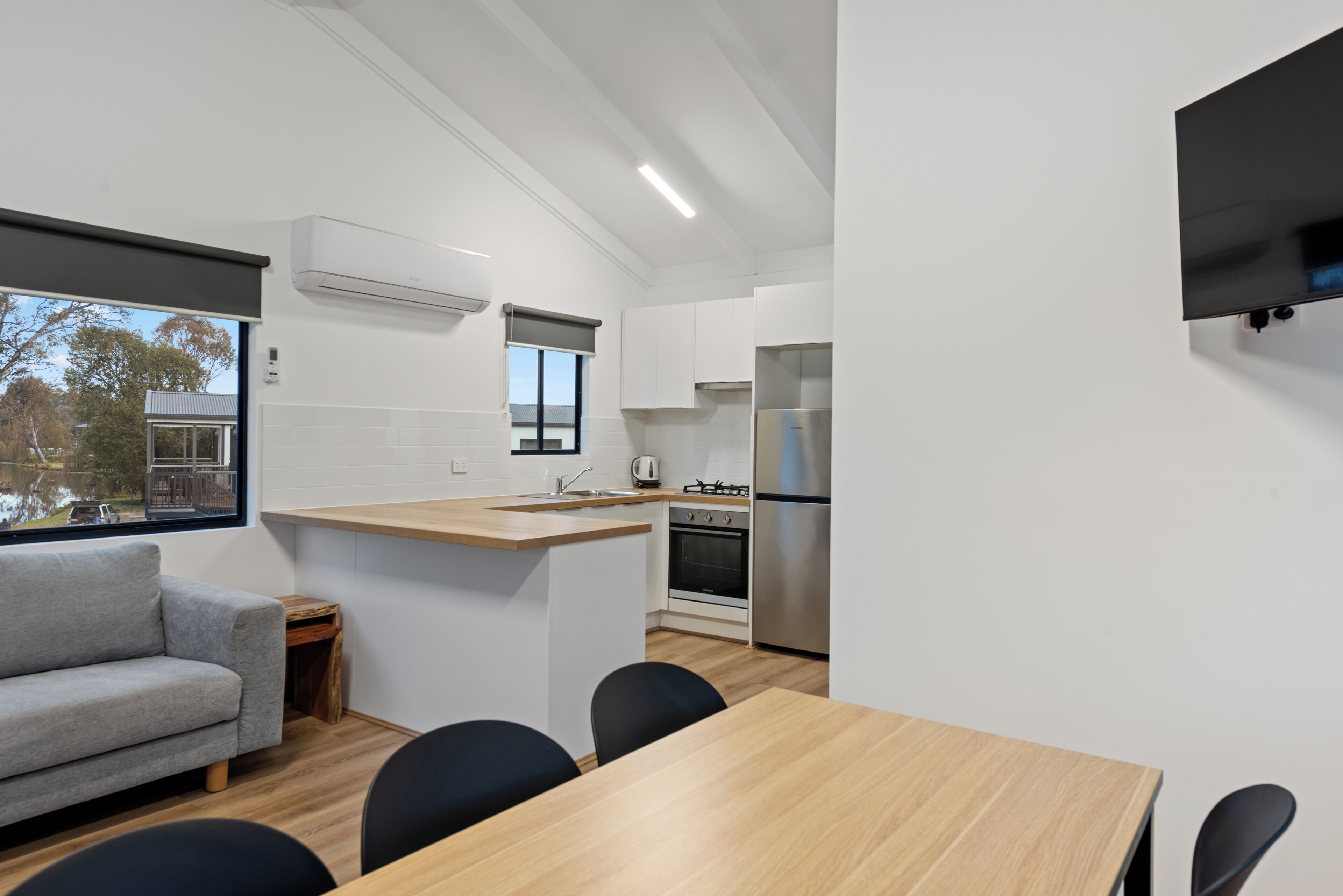 A modern kitchen with a central island, a built-in oven, and a refrigerator. There is a dining area with a table and chairs, and a sofa.