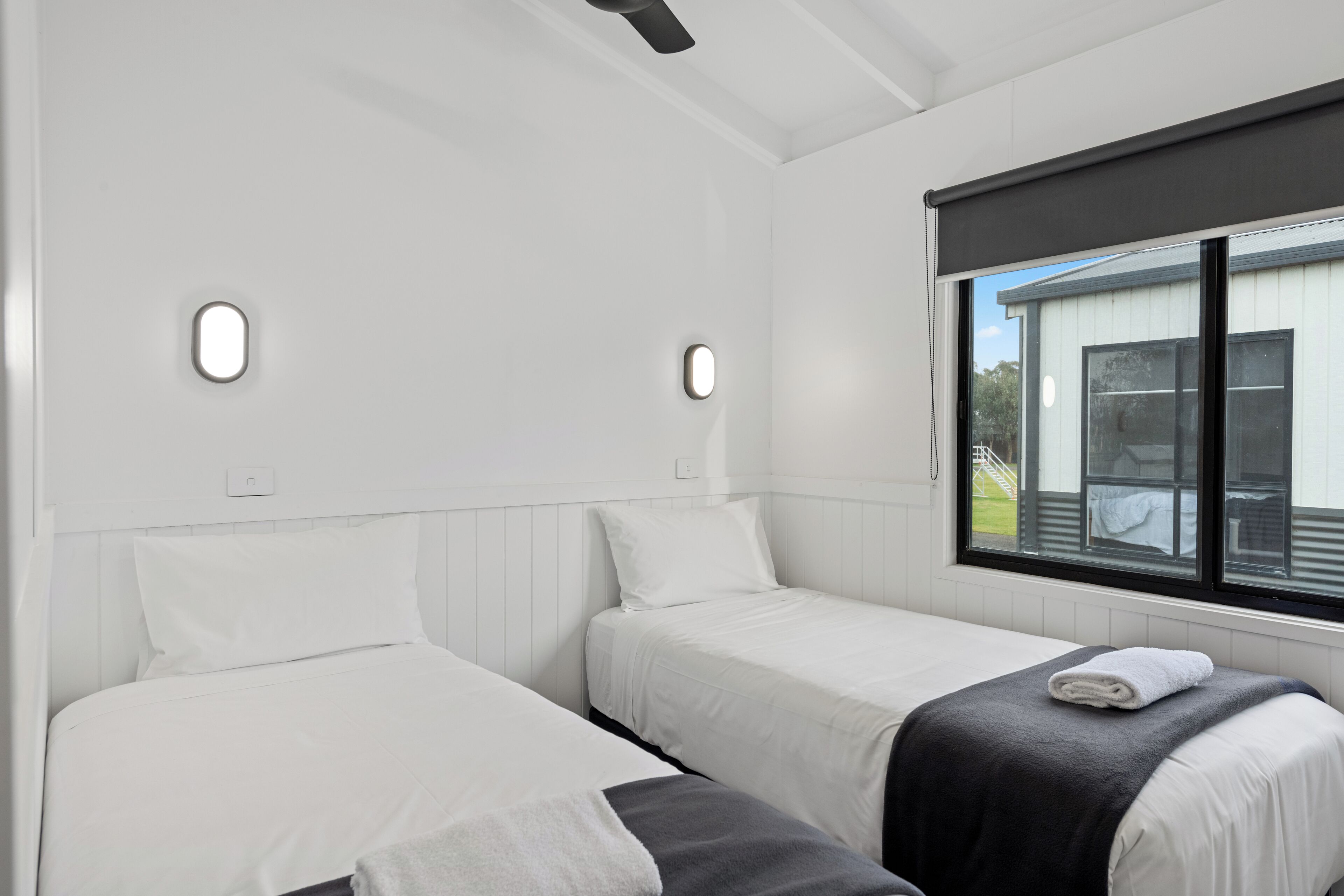 A room with two beds, white bedding, a window with a view, and a ceiling fan.
