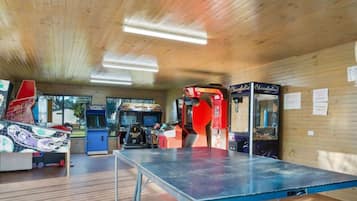 A room with wooden walls and a ceiling, featuring a ping pong table, arcade games, and vending machines.