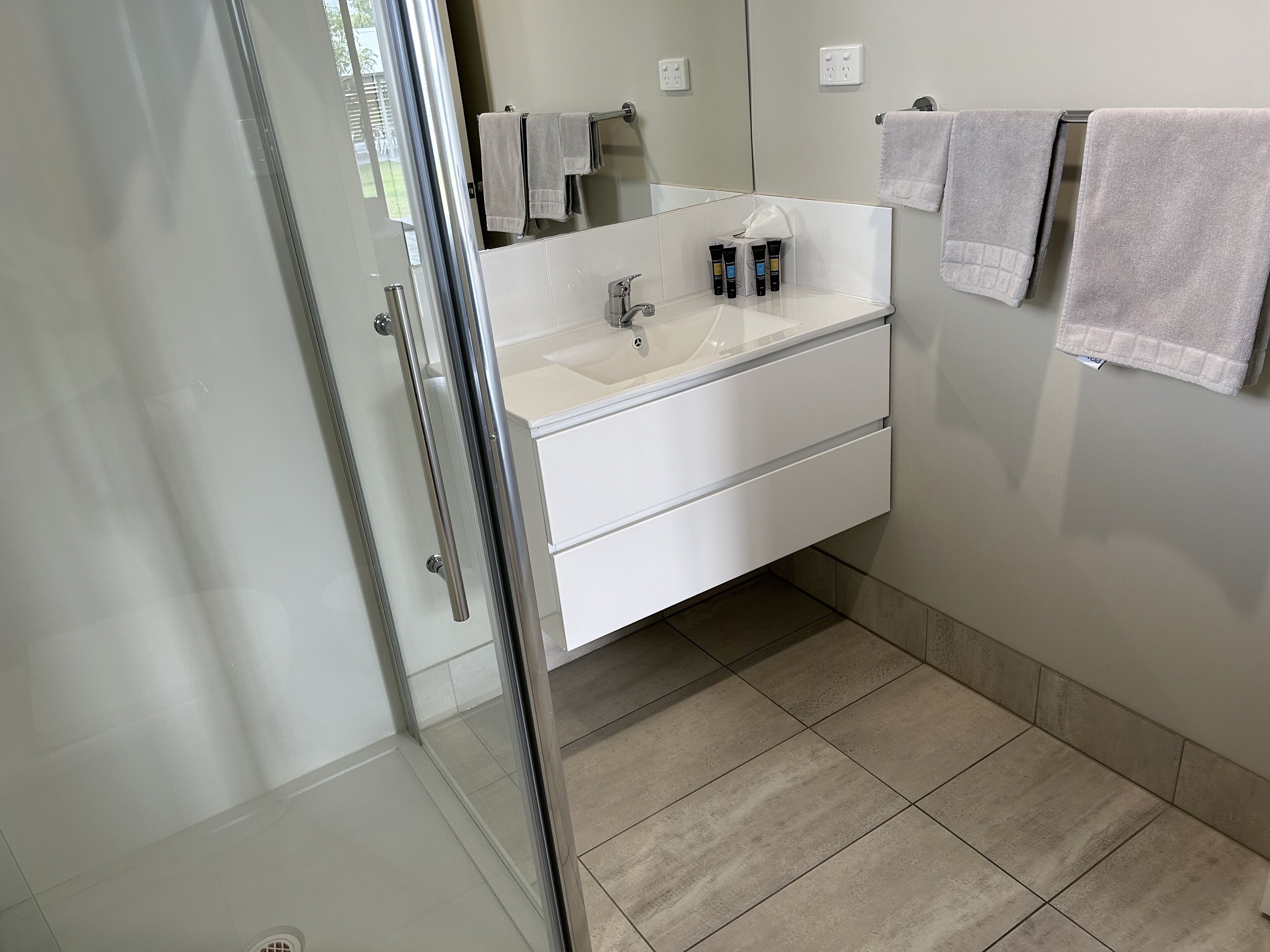 Een moderne badkamer met een glazen douchecabine, een wit wastafelmeubel met spiegel, en twee handdoeken aan de muur.