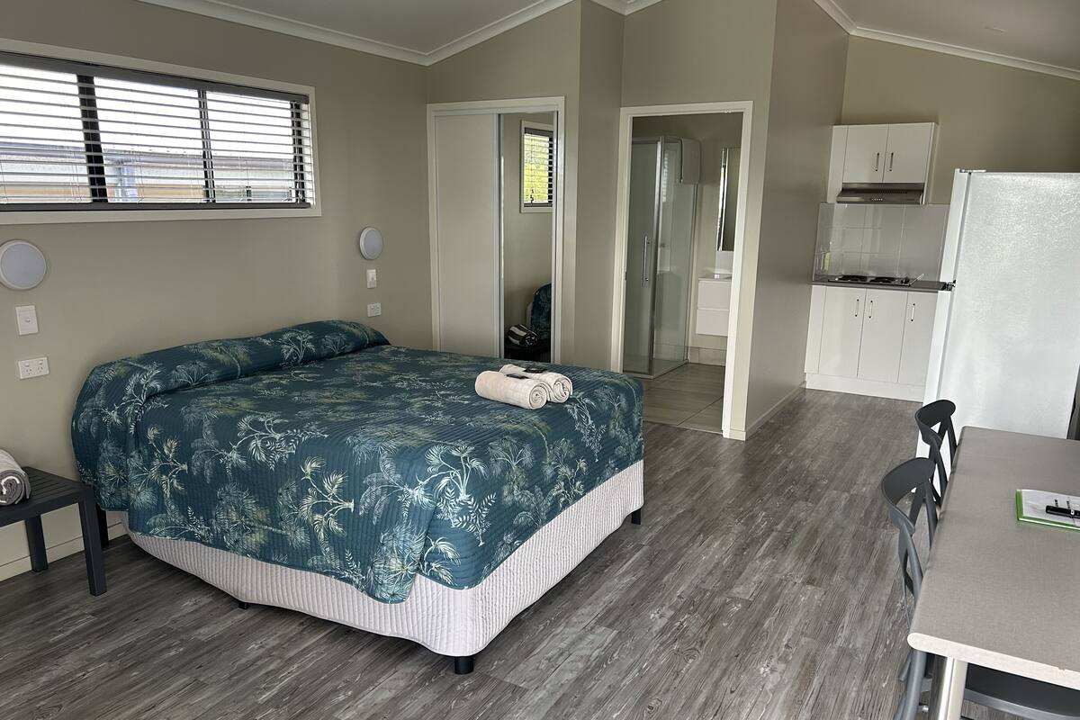 A bedroom with a bed, a desk, and a kitchenette.
