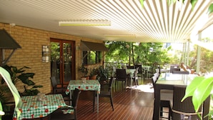 An outdoor patio with tables and chairs, covered by a roof, and surrounded by greenery. - Barcaldine Country Motor Inn (Barcaldine)
