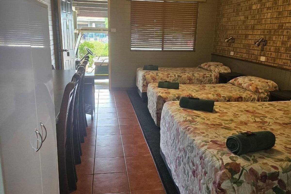 A corridor with three beds, a tiled floor, a brick wall, and a ceiling light.