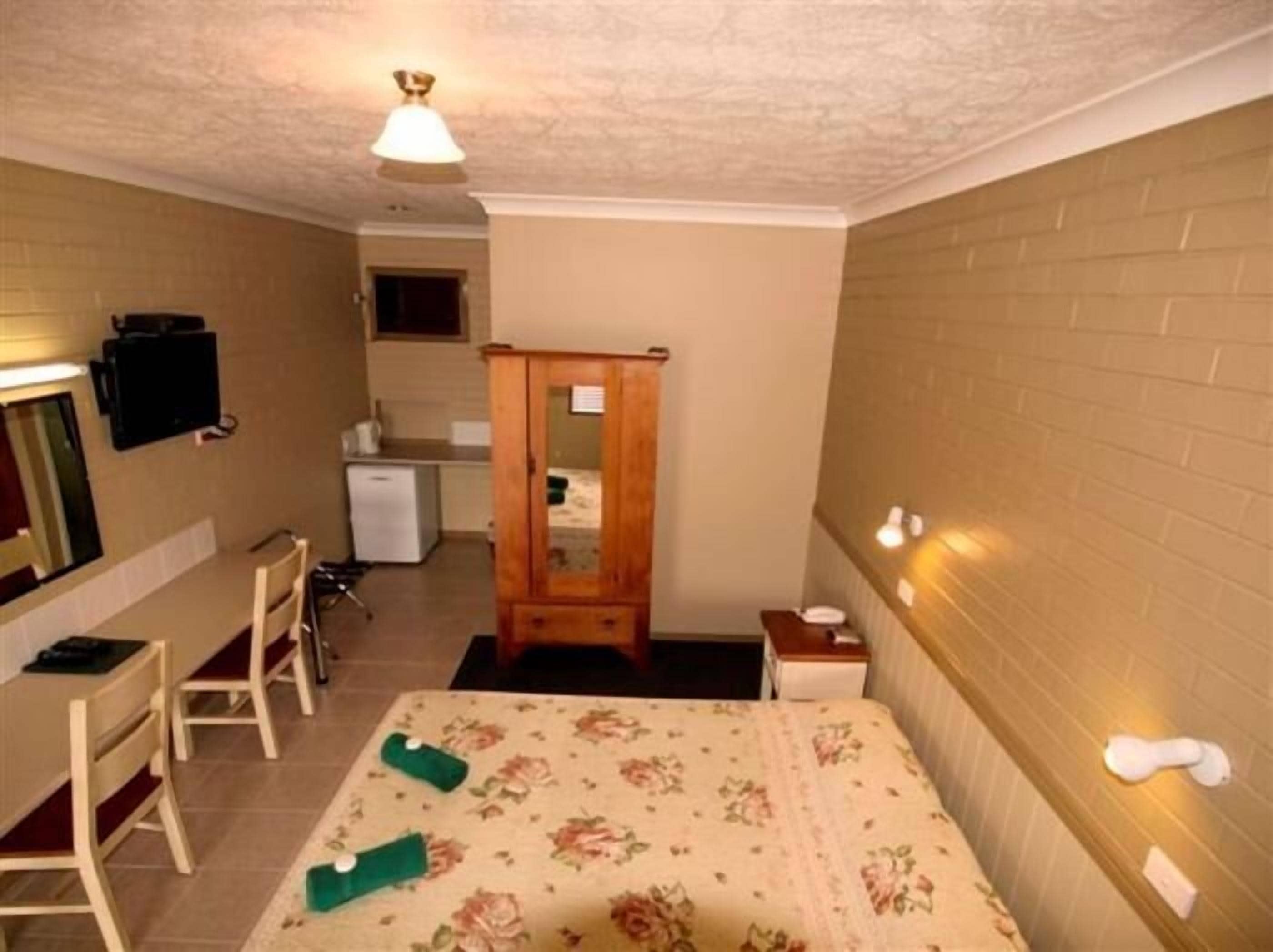 A small, compact room with a bed, a desk, a chair, a wardrobe, and a small kitchenette.