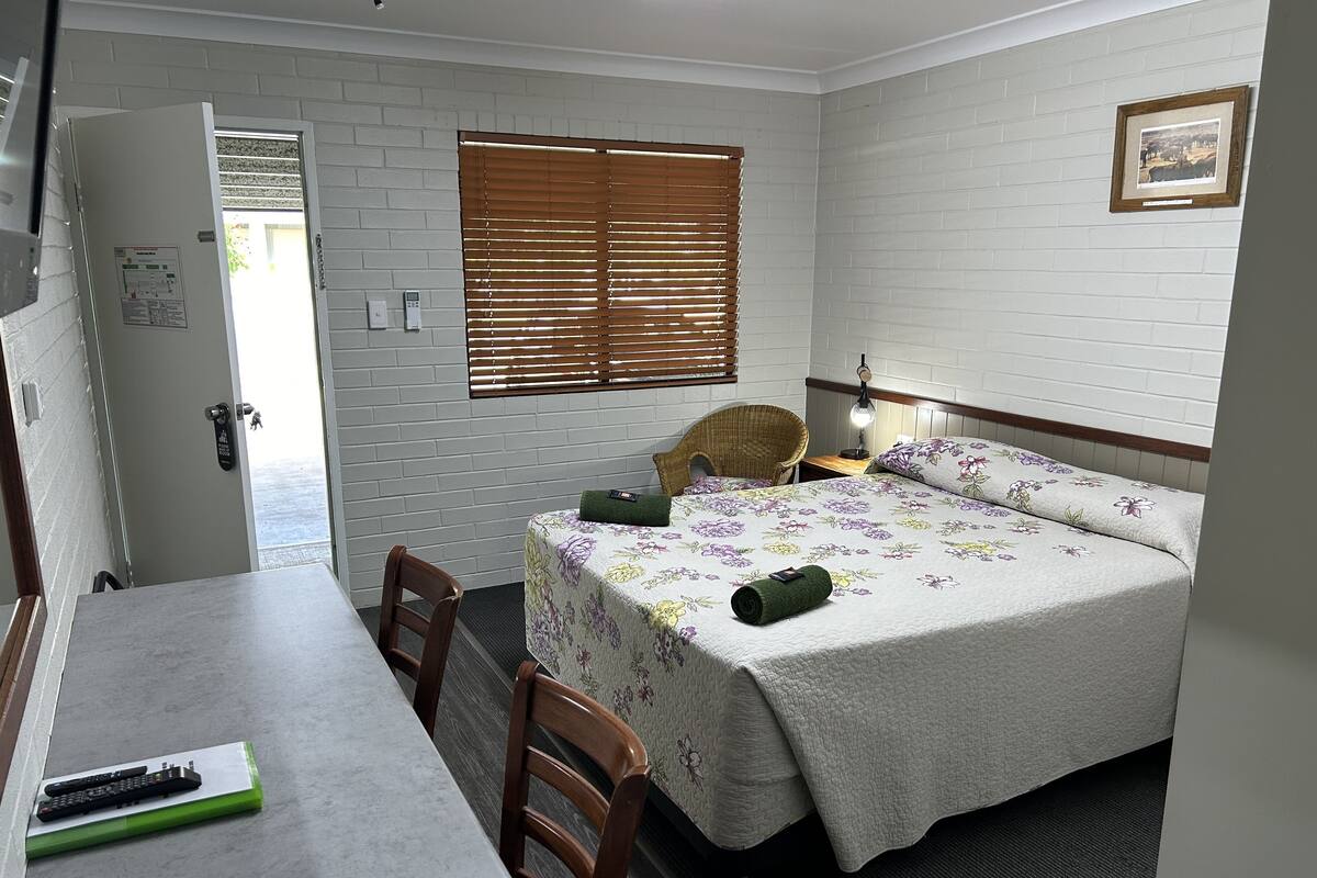 A bedroom with a bed, a chair, a table, and a window with blinds.