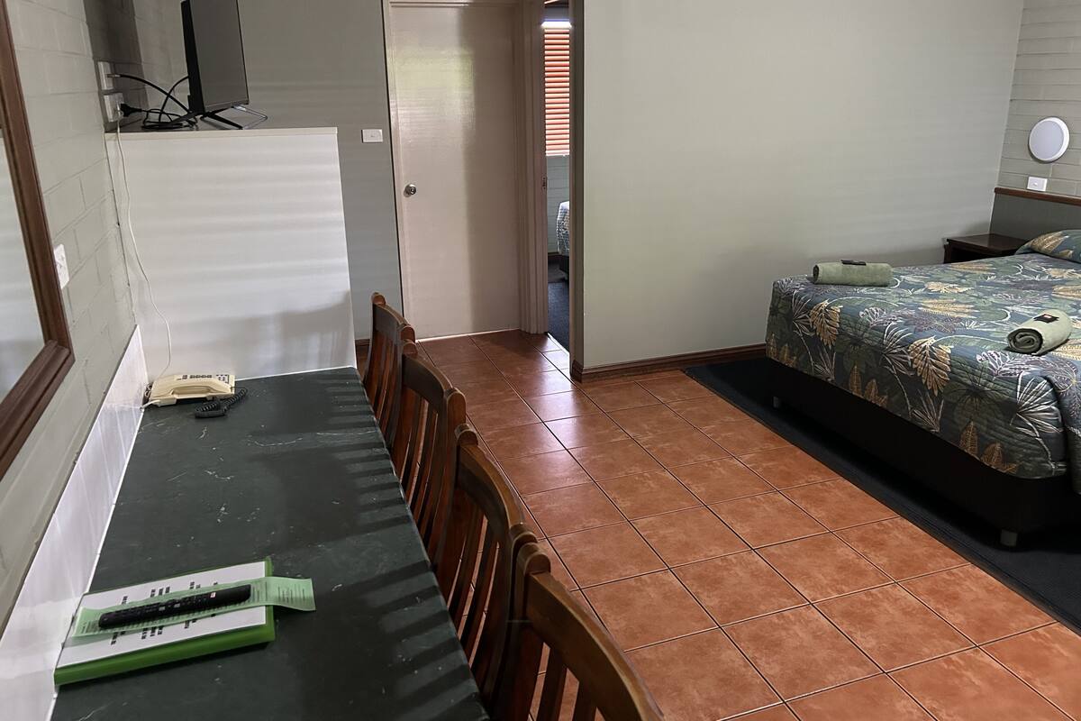 A hotel room with a dining table, chairs, a bed with a floral bedspread, and a view of the hallway.