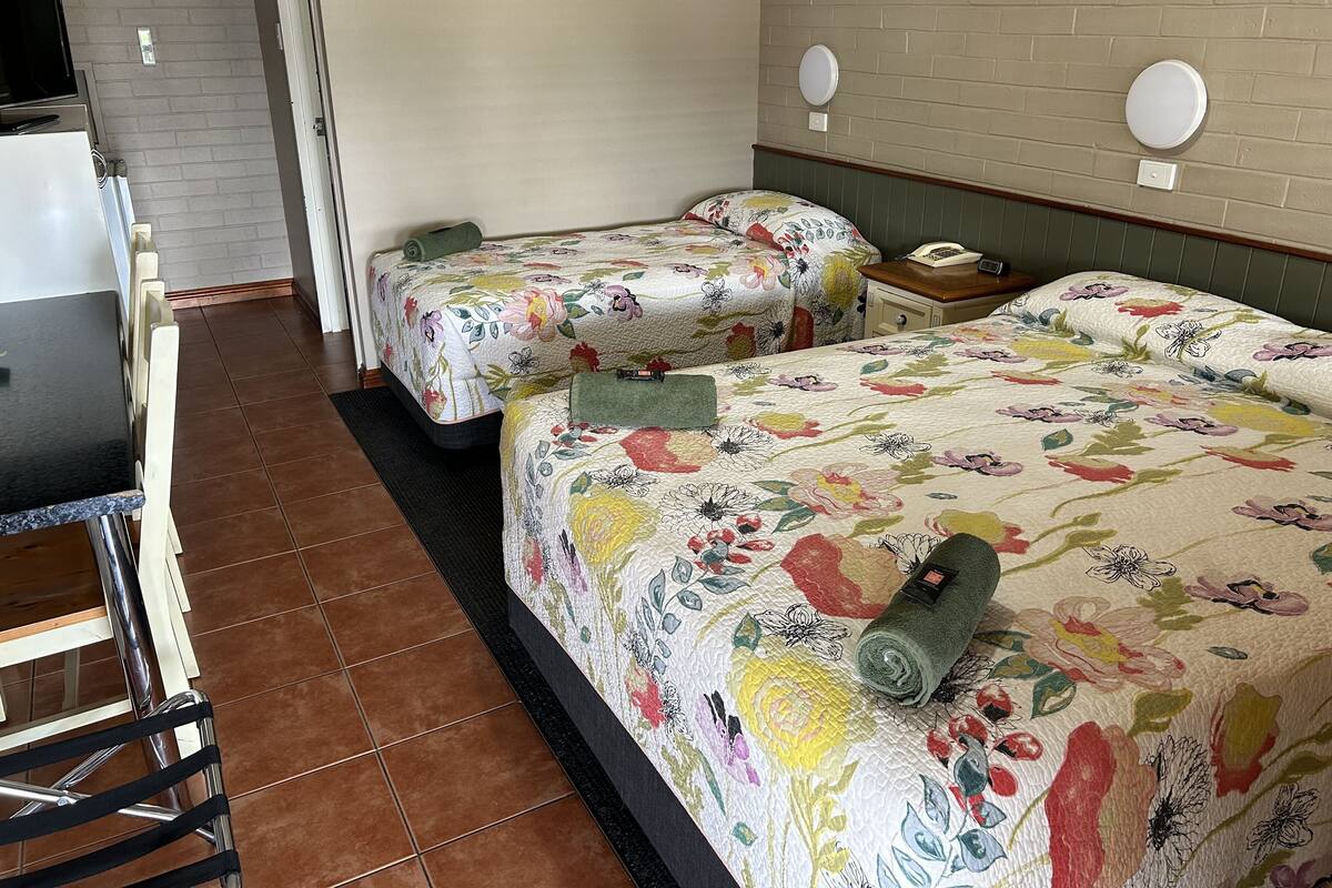 A hotel room with two beds, a small table, and a chair. There are two bedside tables with lamps.