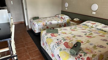 A hotel room with two beds, a small table, and a chair. There are two bedside tables with lamps.