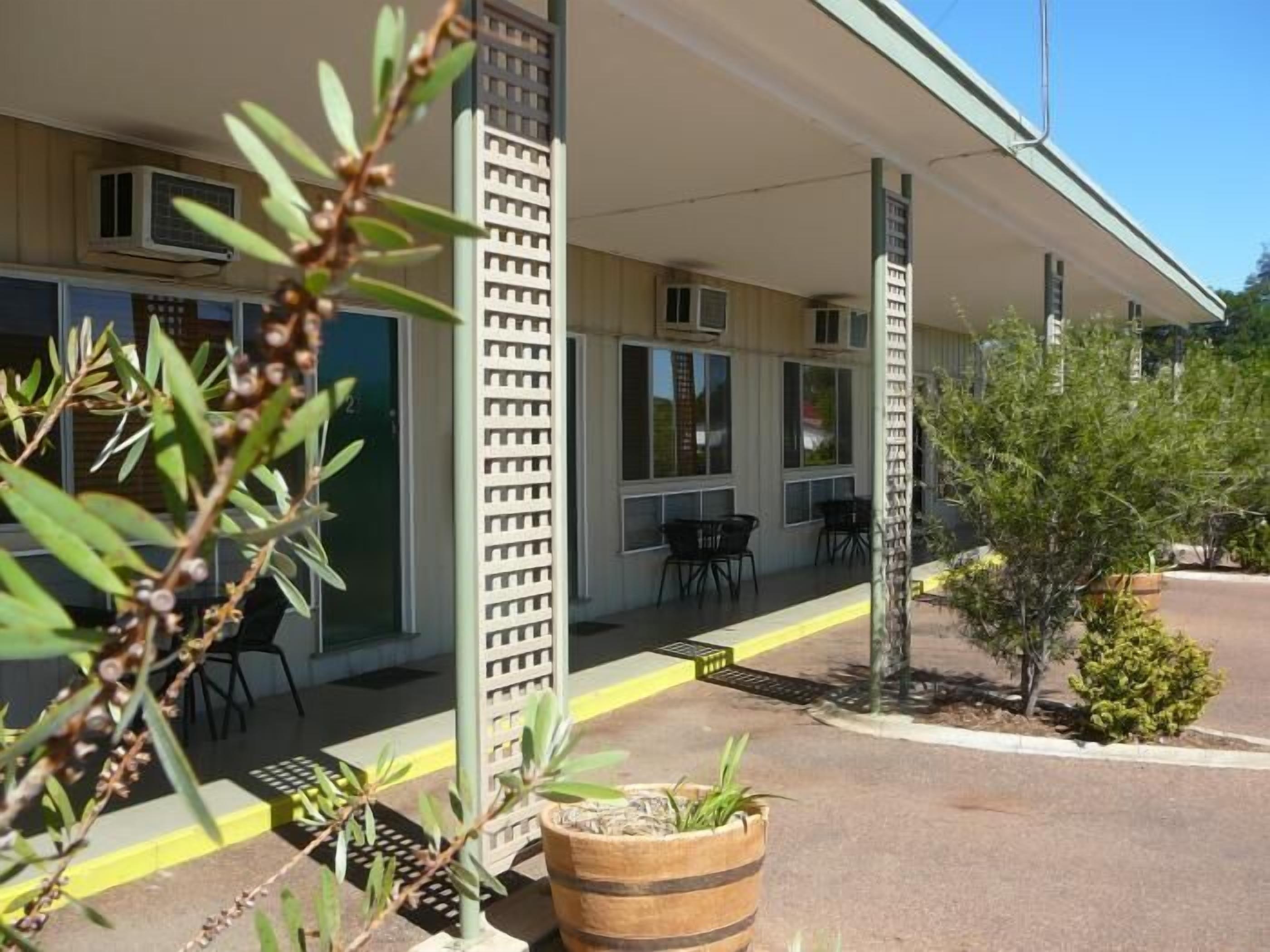 A building with a covered outdoor seating area, a wooden barrel planter, and a small tree.
