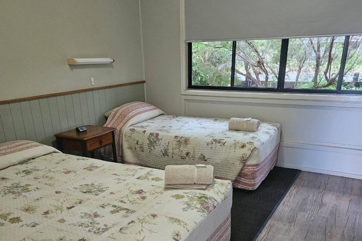 A hotel room with two beds, a window with a view of trees, and a wooden floor.