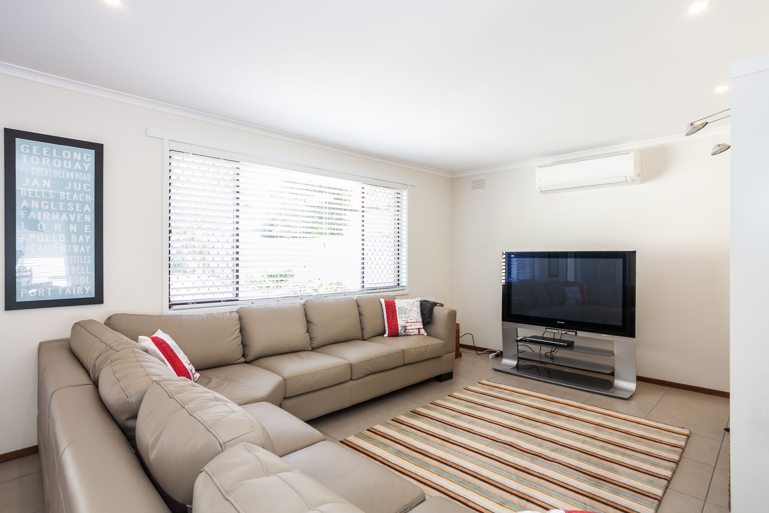 A modern living room with a beige sectional sofa, a flat-screen TV, and a striped rug.