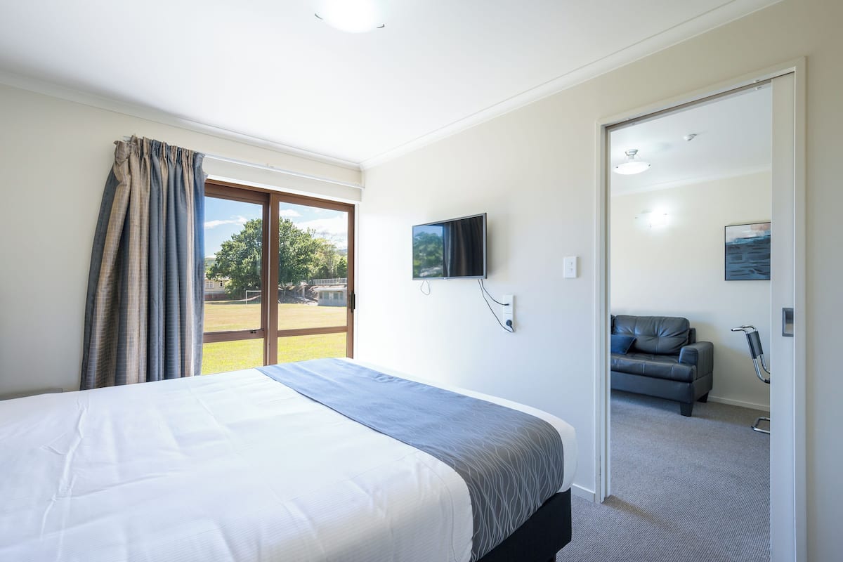 A hotel room with a bed, a TV, a sofa, and a view of the outdoors.