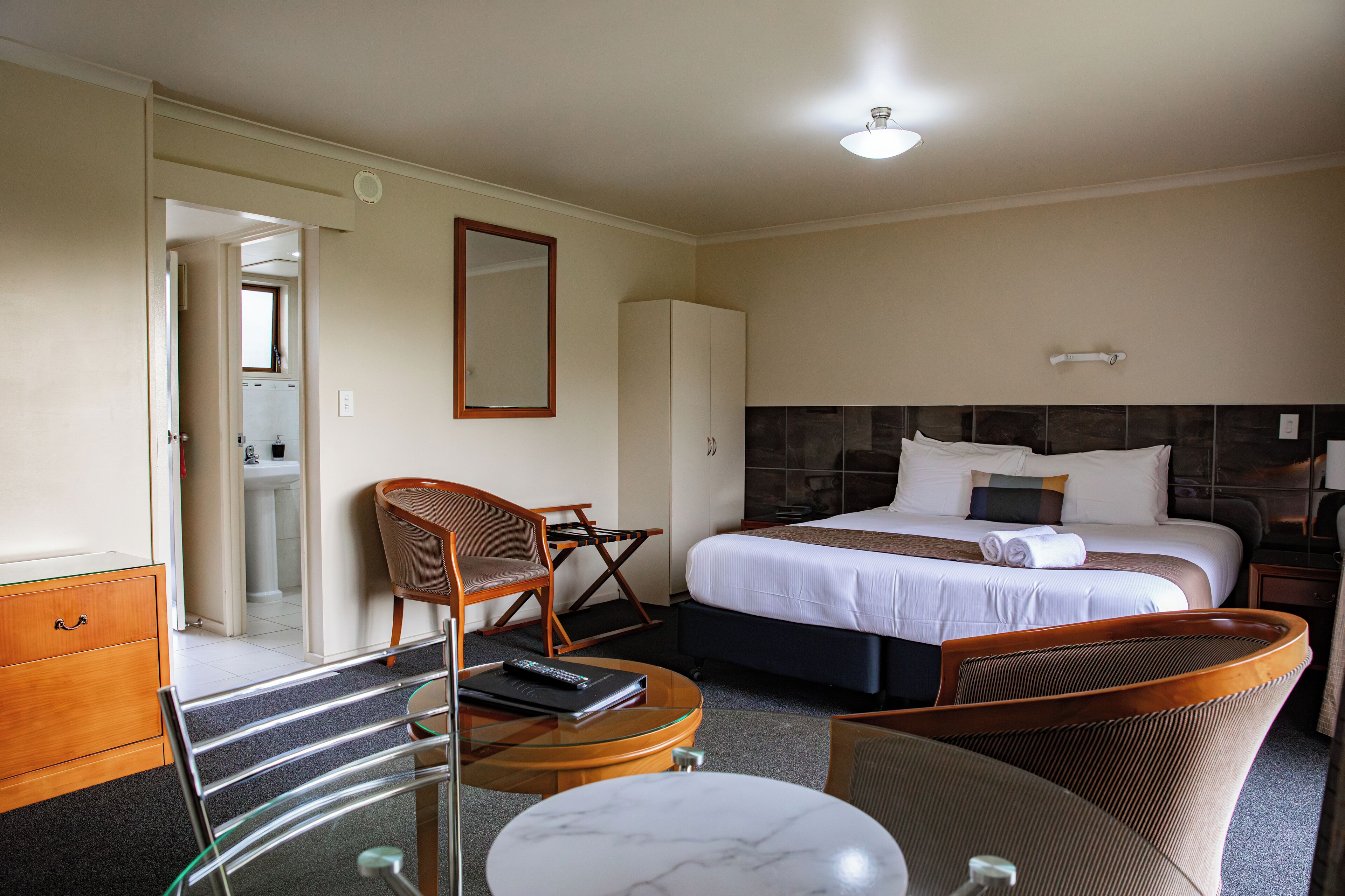 A hotel room with a bed, a chair, a desk, a mirror, and a wardrobe.