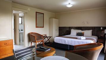 A hotel room with a bed, a chair, a desk, a mirror, and a wardrobe.