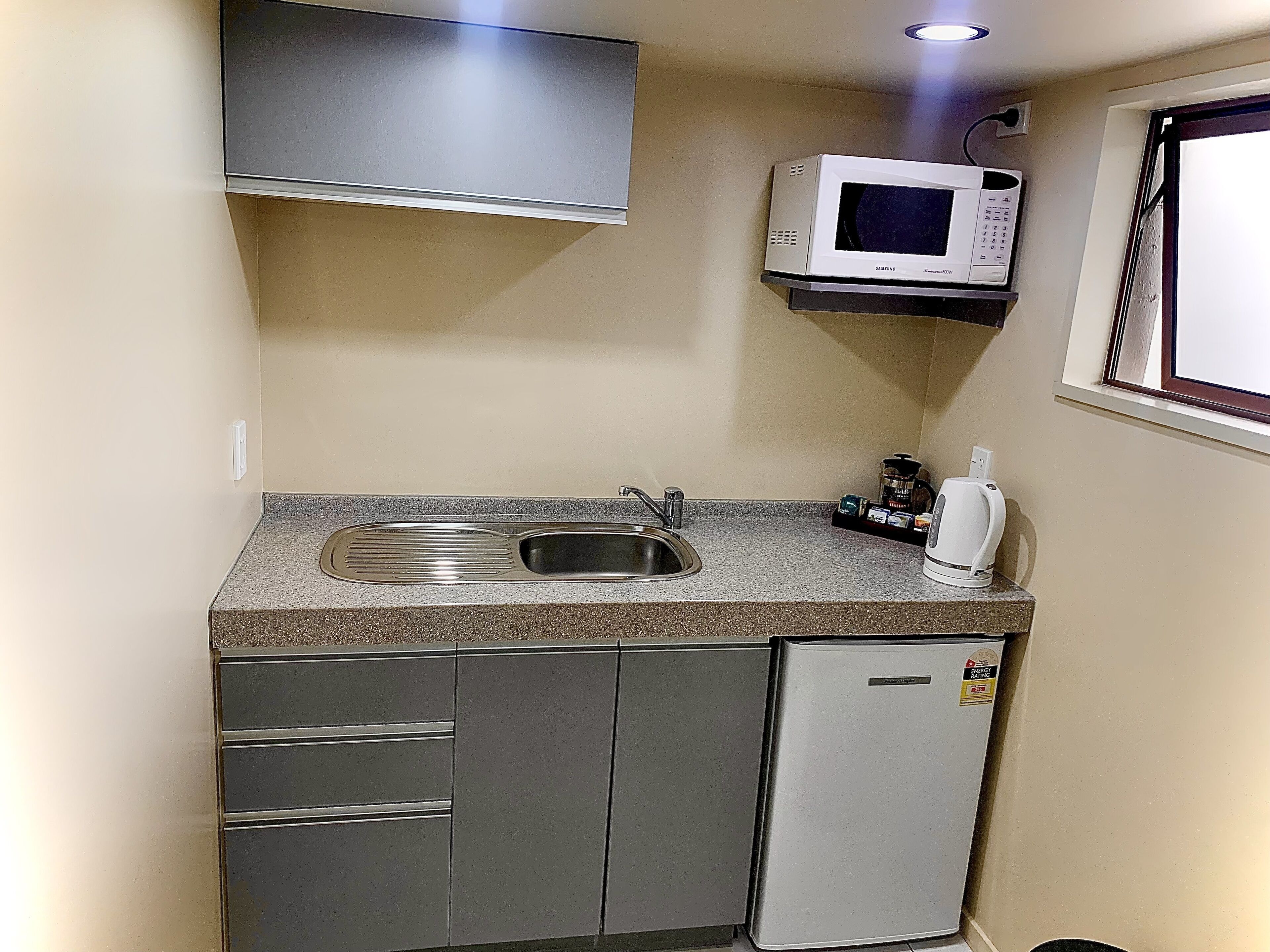 A compact kitchen with a built-in sink, a microwave, a small refrigerator, and a coffee maker.