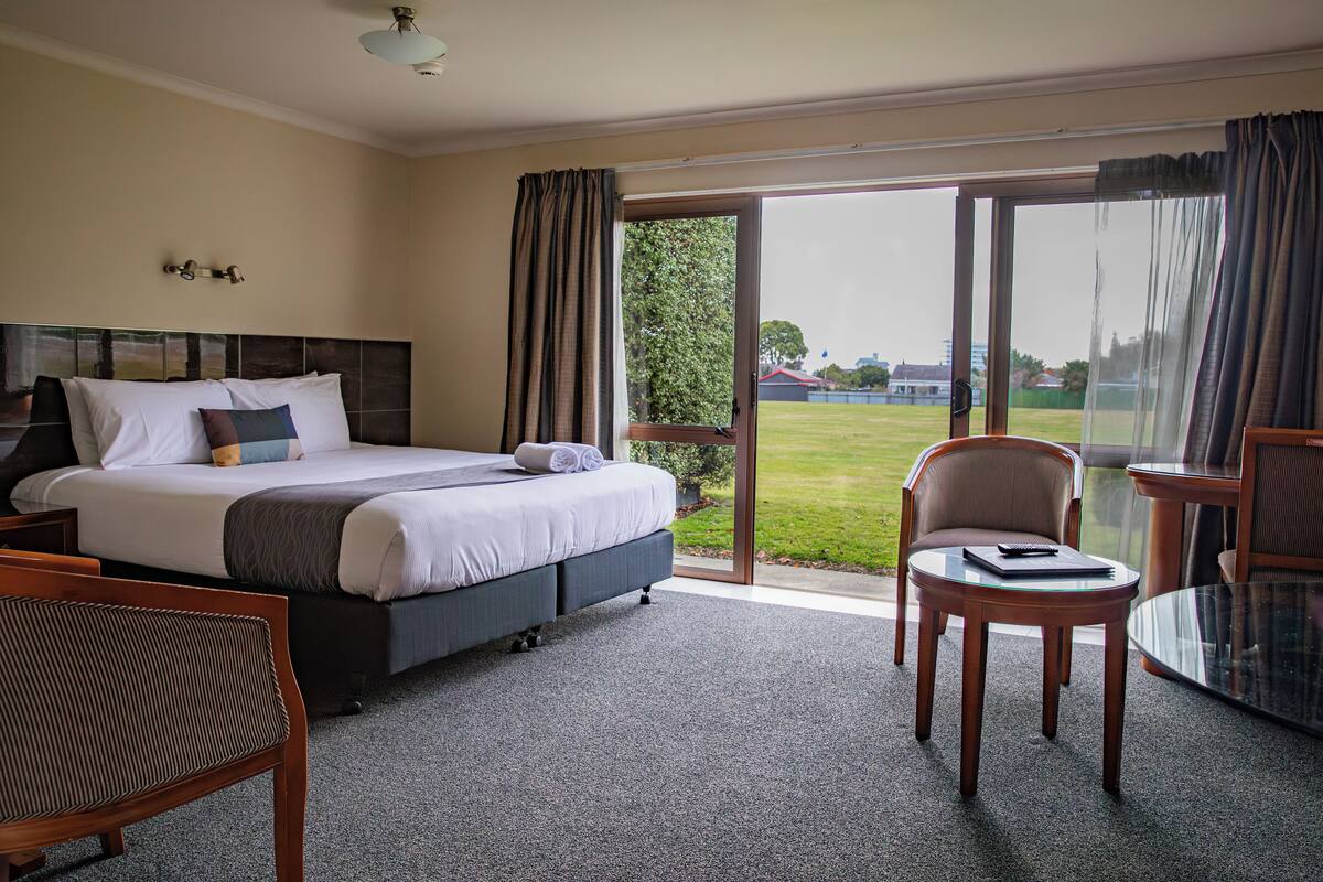 A hotel room with a large bed, a chair, a small table, and a view of the outdoors.
