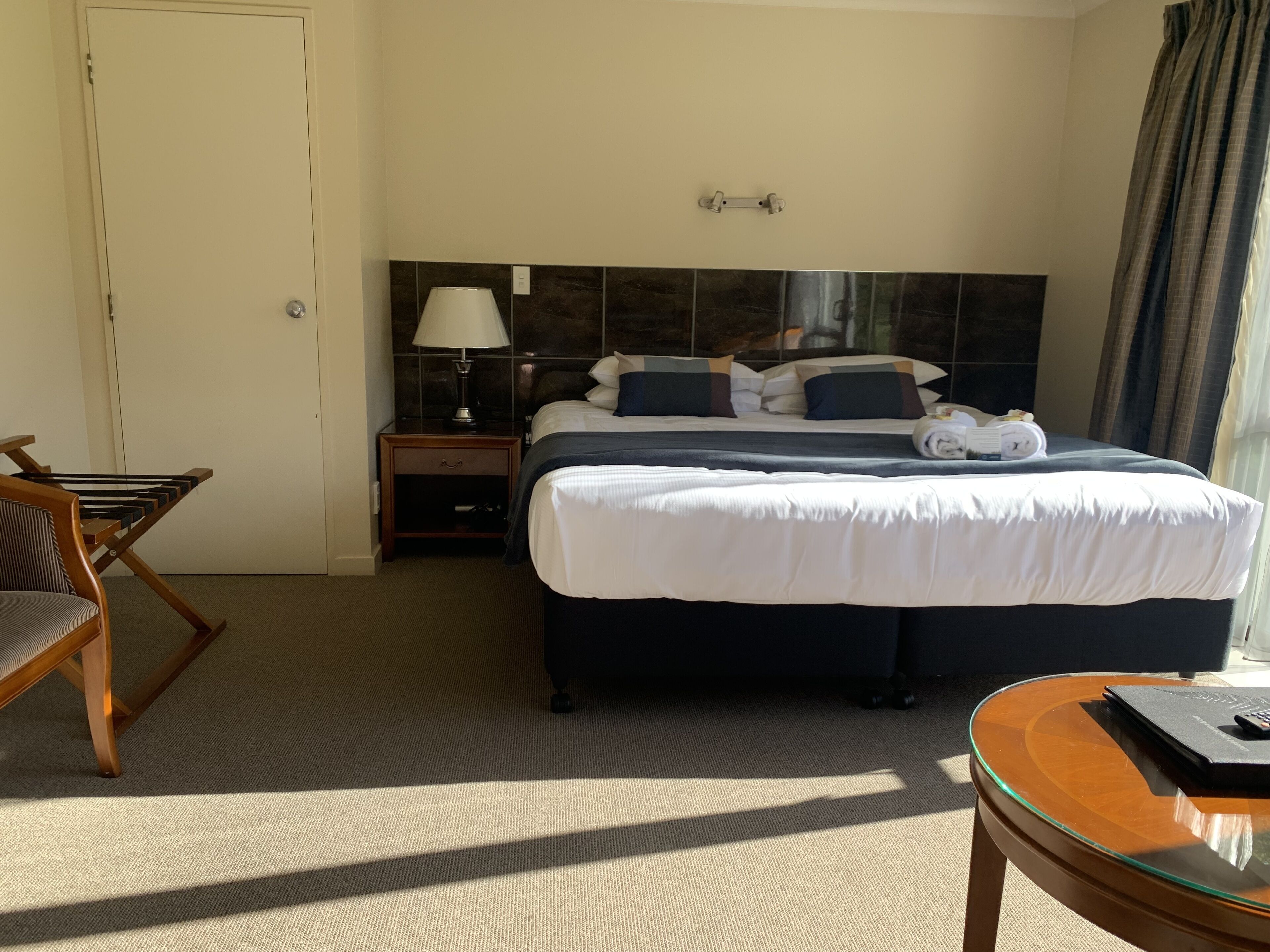 Una habitación de hotel con cama, mesita de noche, lámpara, silla y una pequeña mesa.