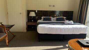 Una habitación de hotel con cama, mesita de noche, lámpara, silla y una pequeña mesa.