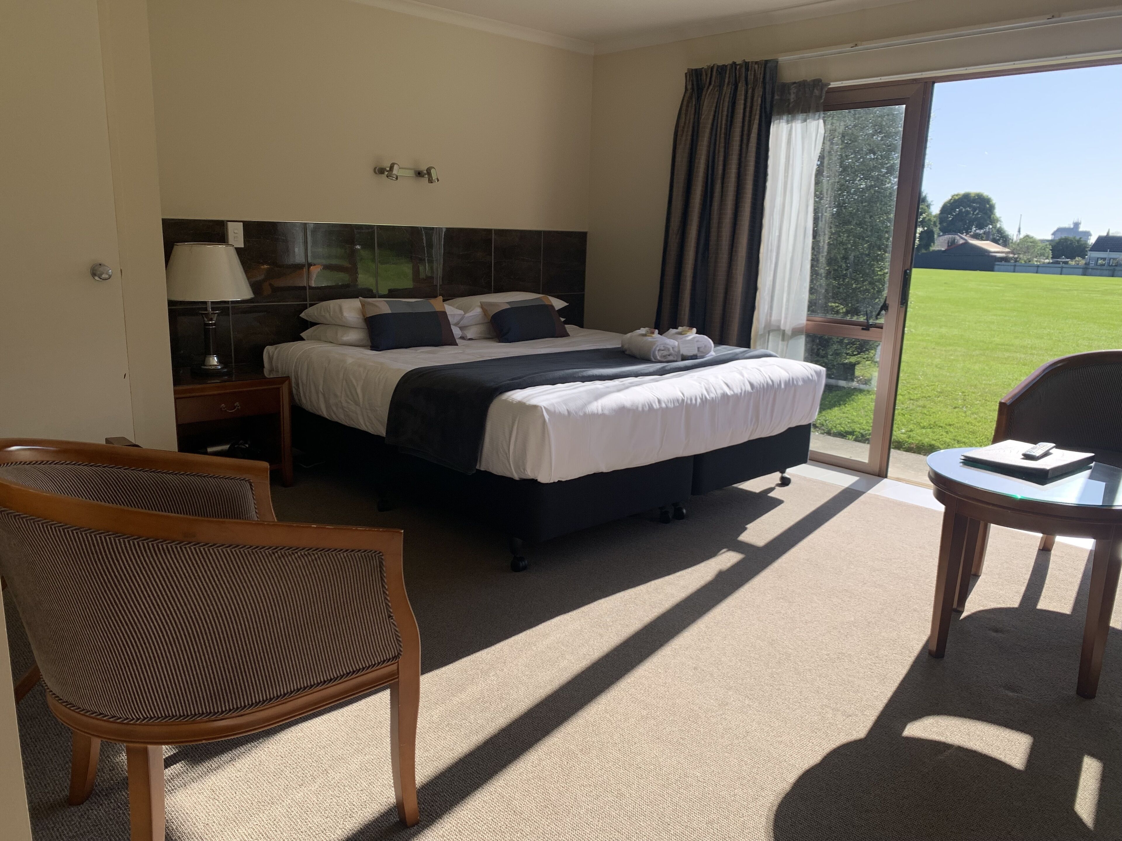 Habitación de hotel con una cama grande, un escritorio, una silla y vistas a un paisaje verde a través del ventanal.