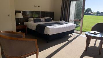 Habitación de hotel con una cama grande, un escritorio, una silla y vistas a un paisaje verde a través del ventanal.