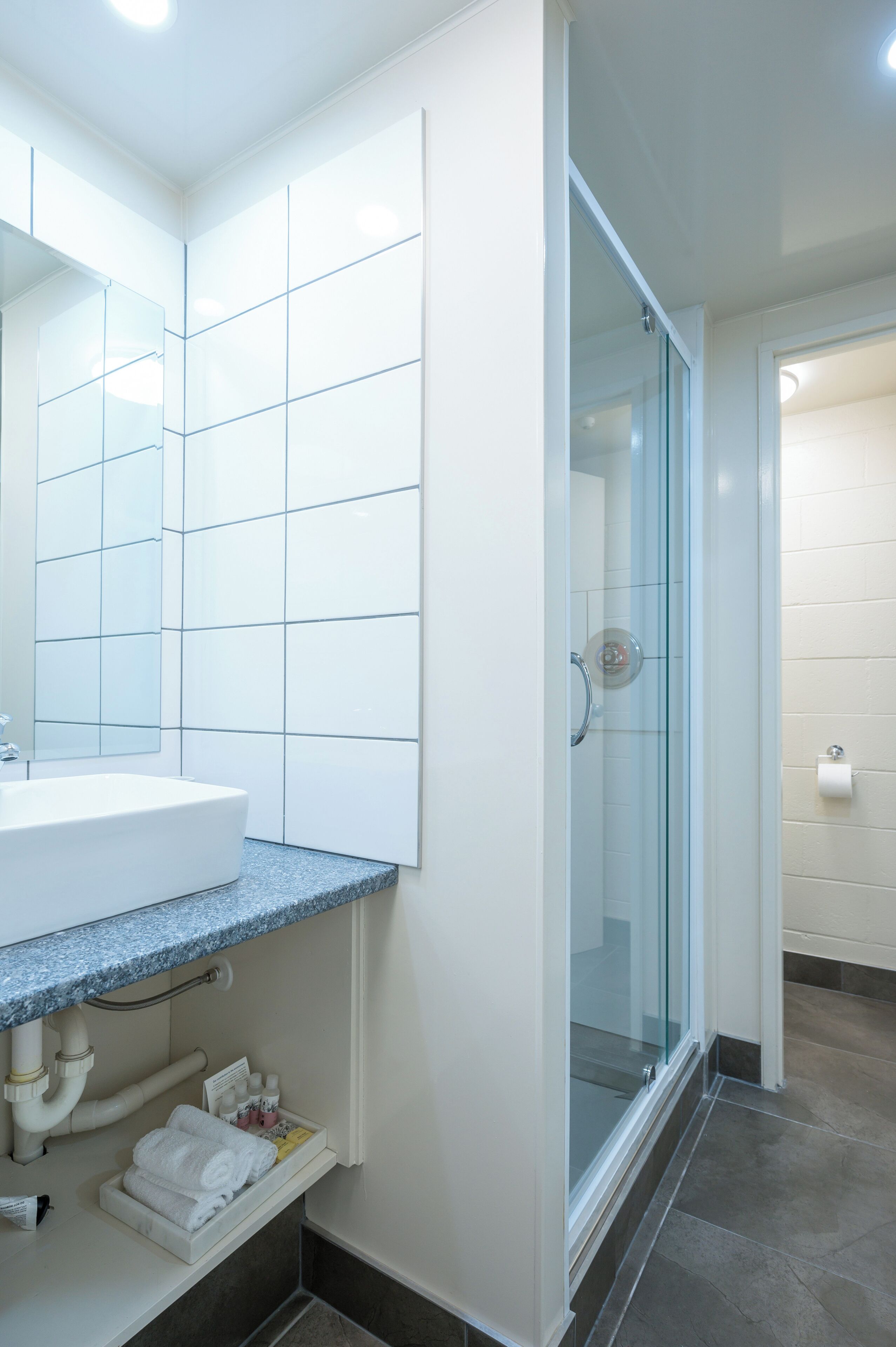 Un baño moderno con un lavabo blanco, cabina de ducha con paredes de vidrio y suelo de baldosas.