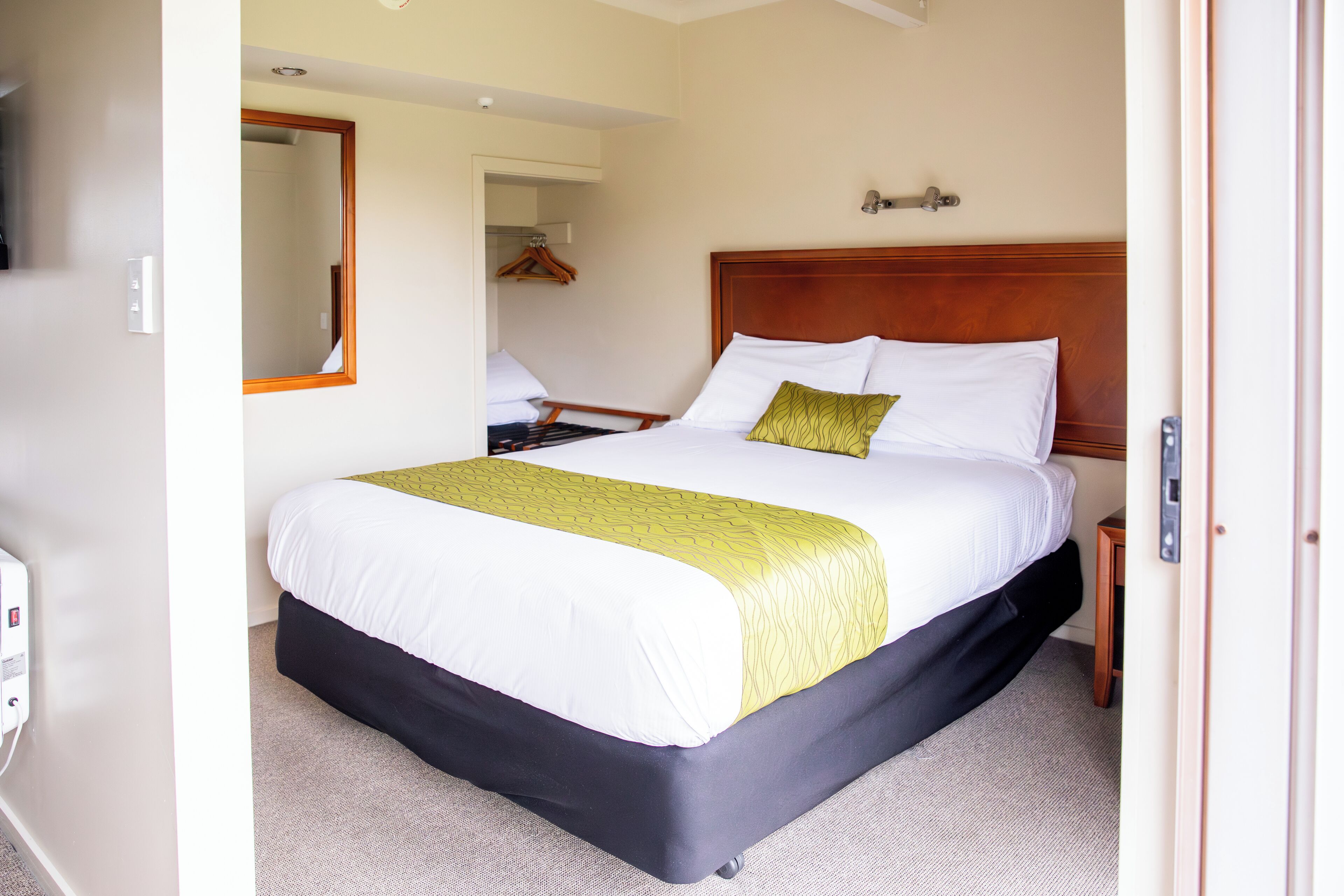 A hotel room with a large bed, a wooden headboard, a bedside table, and a mirror on the wall.