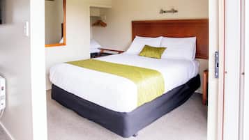A hotel room with a large bed, a wooden headboard, a bedside table, and a mirror on the wall.