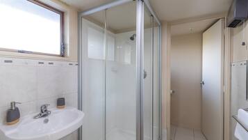 Un baño moderno con cabina de ducha de vidrio, un lavamanos con dos dispensadores de jabón y una ventana sobre el lavamanos.