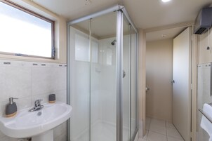 Un baño moderno con cabina de ducha de vidrio, un lavamanos con dos dispensadores de jabón y una ventana sobre el lavamanos.