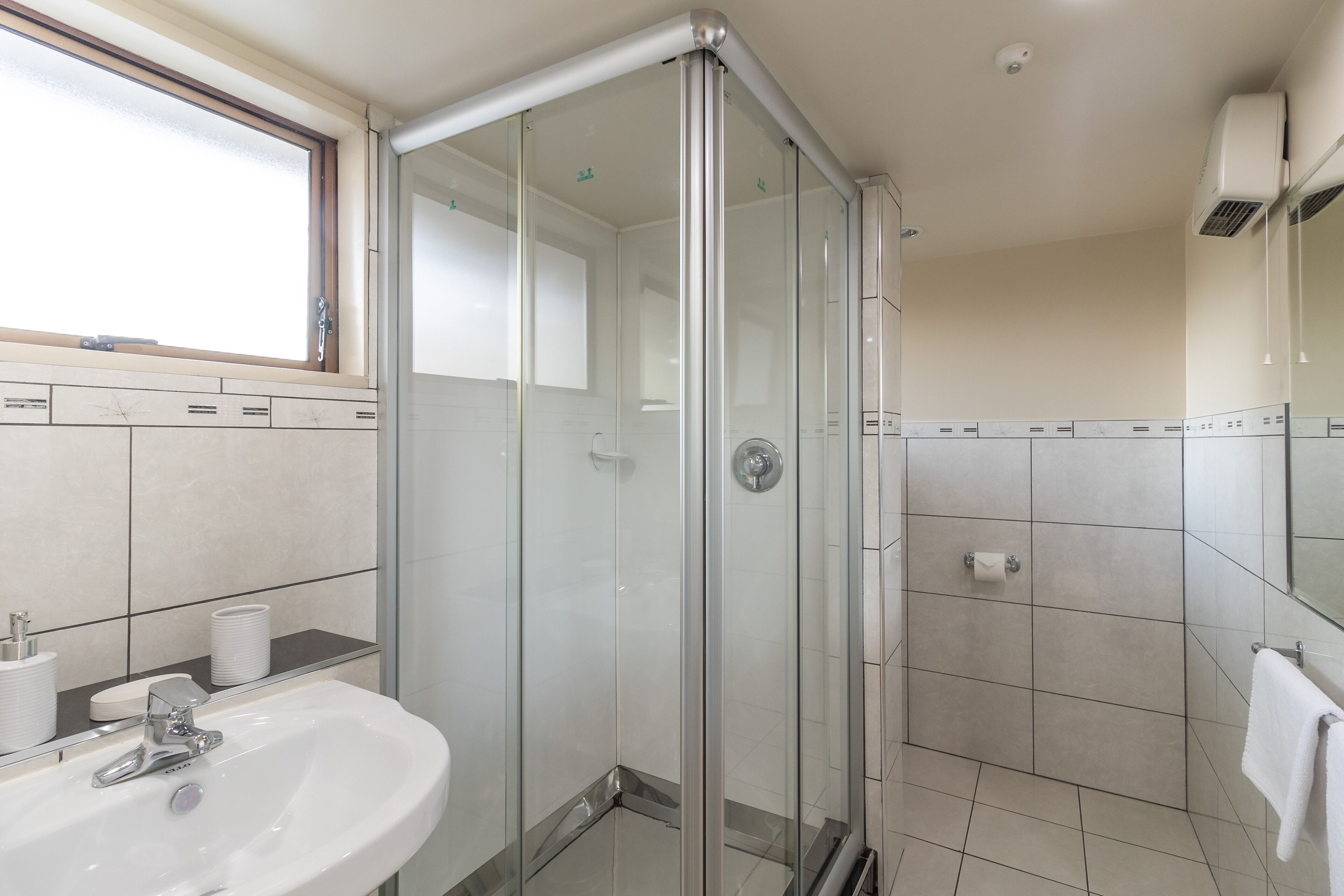 Une salle de bain moderne avec une douche à parois de verre, un lavabo avec un miroir et une fenêtre au-dessus du lavabo.