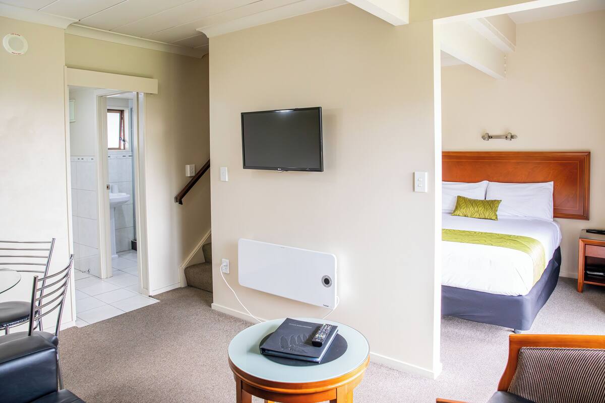 A hotel room with a bed, a TV mounted on the wall, a small table with a remote control, and a chair.