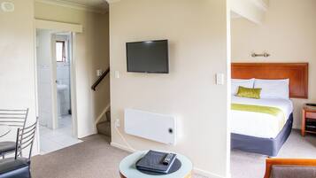 Una habitación de hotel con una cama, un televisor fijado a la pared, una mesita con un control remoto y una silla.