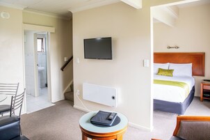 Una habitación de hotel con una cama, un televisor fijado a la pared, una mesita con un control remoto y una silla.