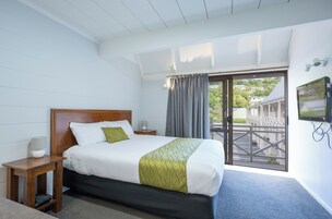 Habitación de hotel con cama, mesita de noche, televisor y vistas al exterior.