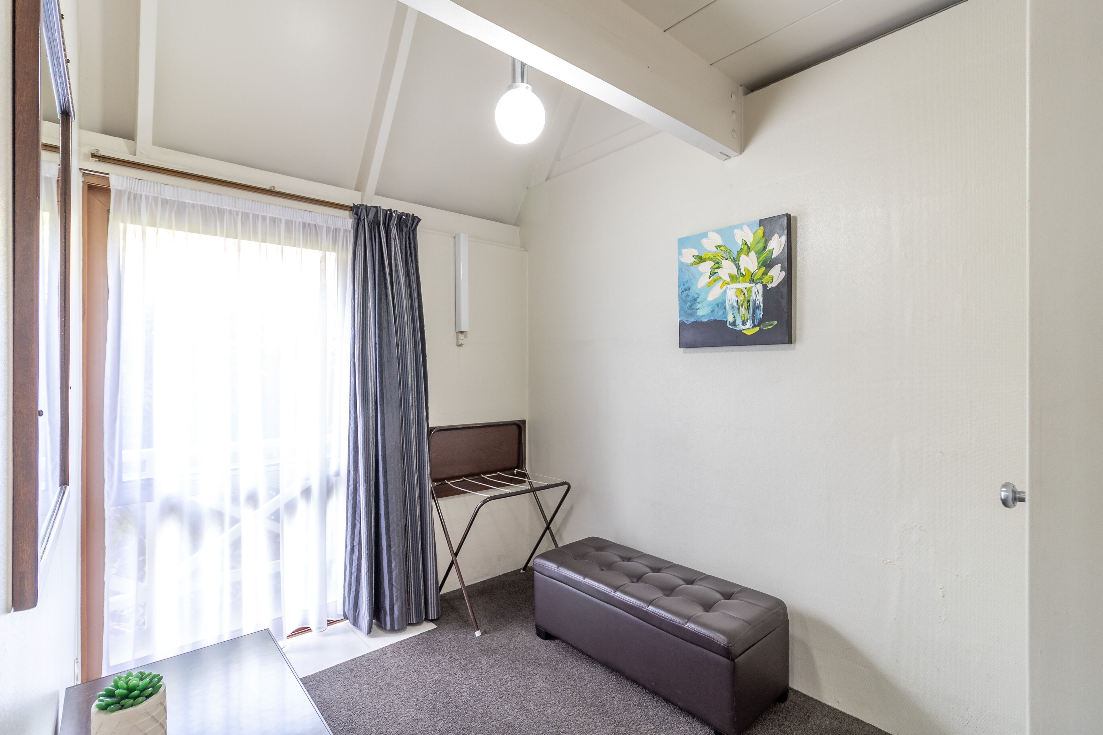 A room with a bed, a bench, a drying rack, and a painting on the wall.