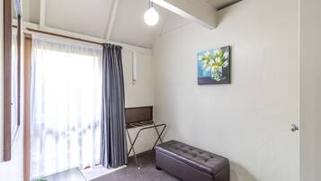 A room with a bed, a bench, a drying rack, and a painting on the wall.