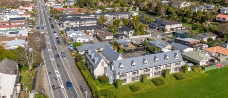 An aerial view of a residential area with houses, a main road, and a large building with a distinct roofline.