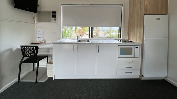 A compact kitchen with a built-in microwave, a refrigerator, a window with a view, and a black chair. - Hi-Way Motel Grafton - Digital & Contactless (South Grafton)
