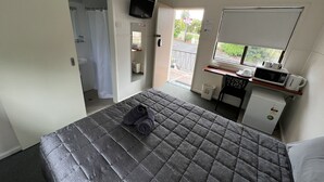 A bedroom with a bed, a desk with a microwave, a TV, and a view of the outside. - Hi-Way Motel Grafton - Digital & Contactless (South Grafton)