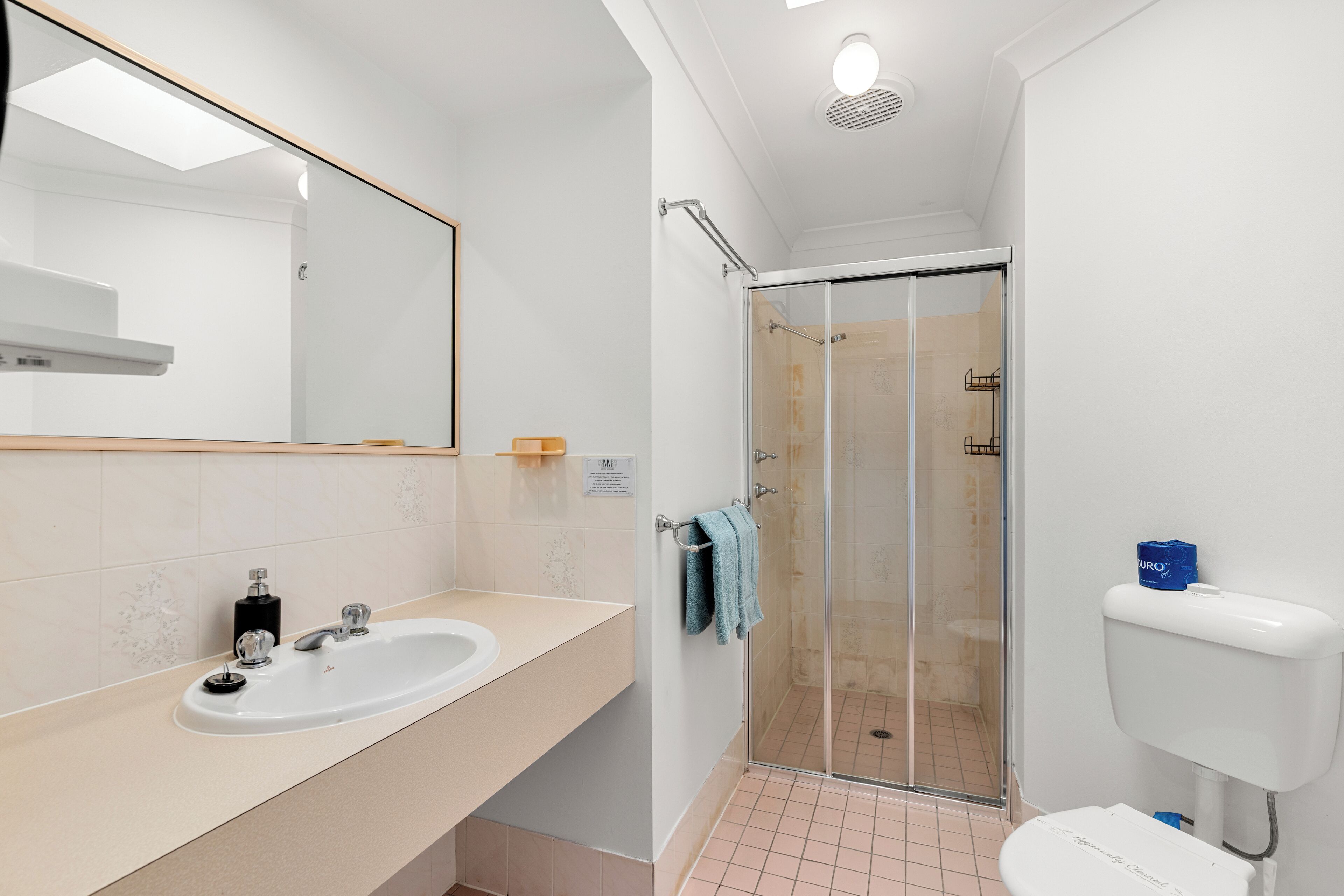 Un baño con lavamanos blanco, espejo y cabina de ducha con paredes de vidrio.