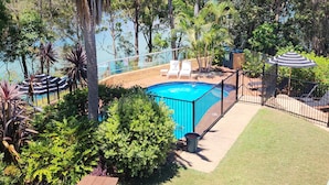 Une piscine entourée d’une végétation luxuriante et d’arbres, avec des chaises longues et des parasols à proximité.