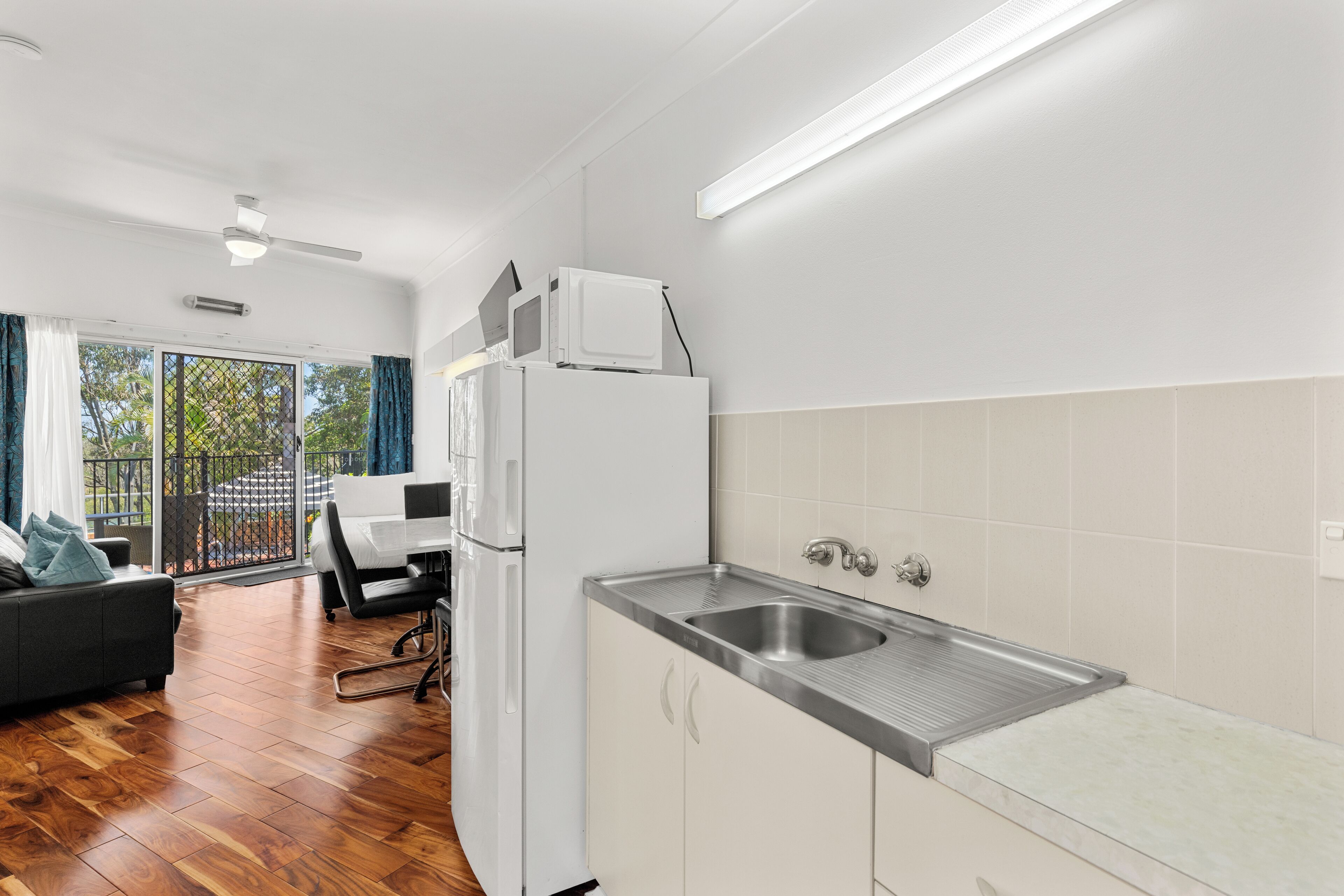 A modern kitchen with a stainless steel sink, white cabinets, and a refrigerator.