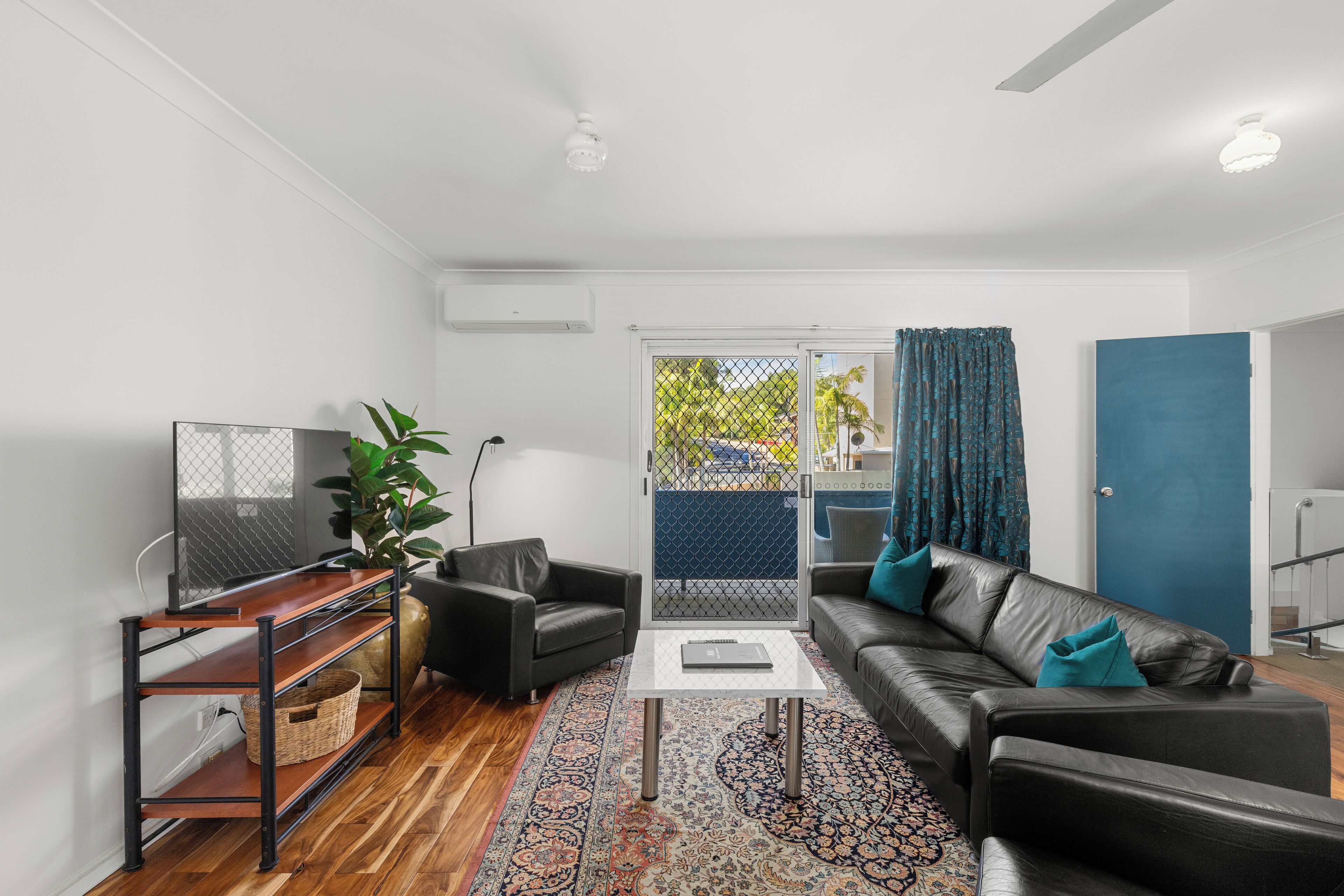 A modern living room with a black leather sofa, a glass coffee table, and a wooden TV stand.