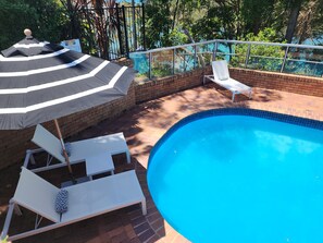 Una piscina al aire libre, sombrillas, sillones reclinables de piscina