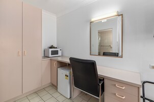 Habitación compacta con kitchenette, microondas, refrigerador, escritorio, silla y espejo.