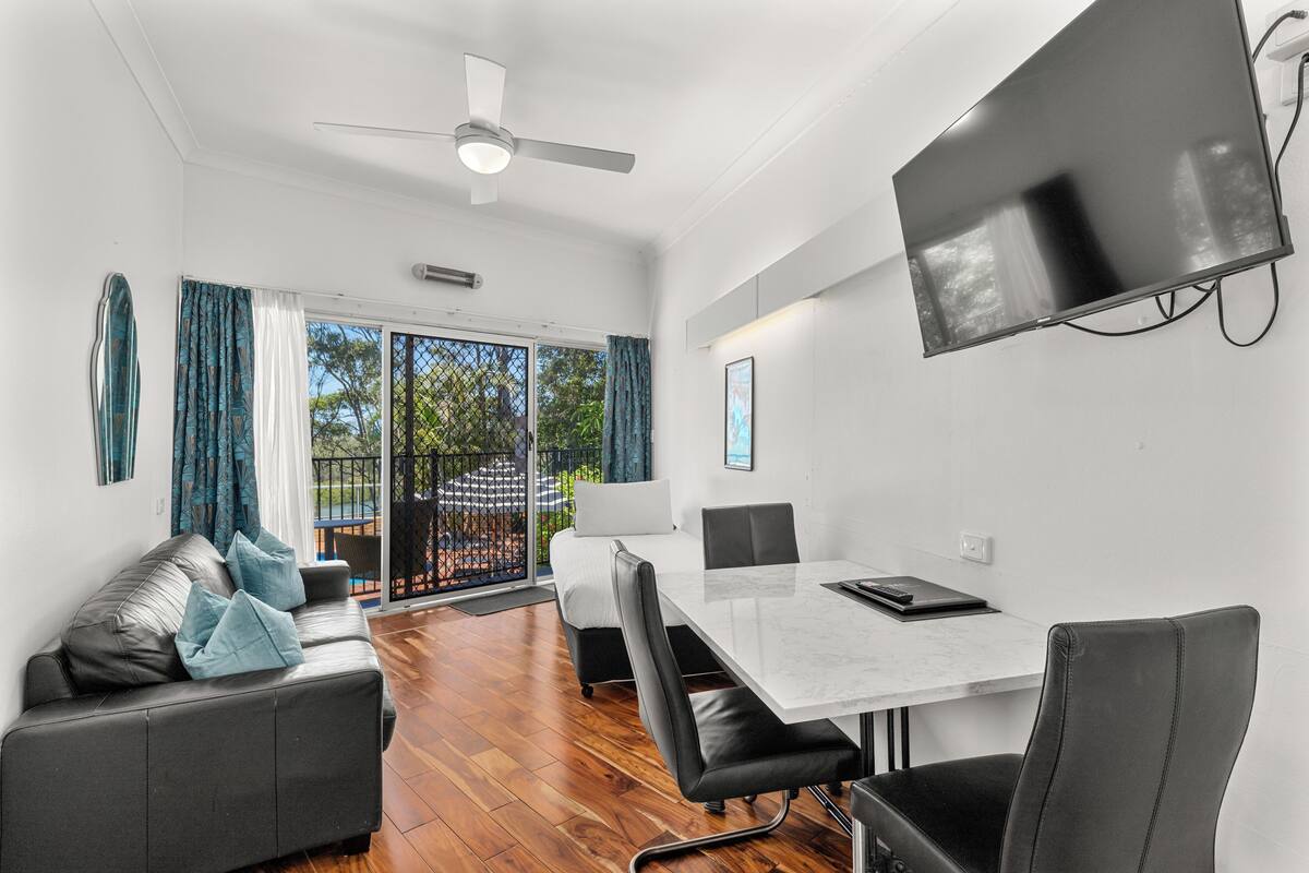 A modern living room with a sofa, a dining table, and a TV mounted on the wall.