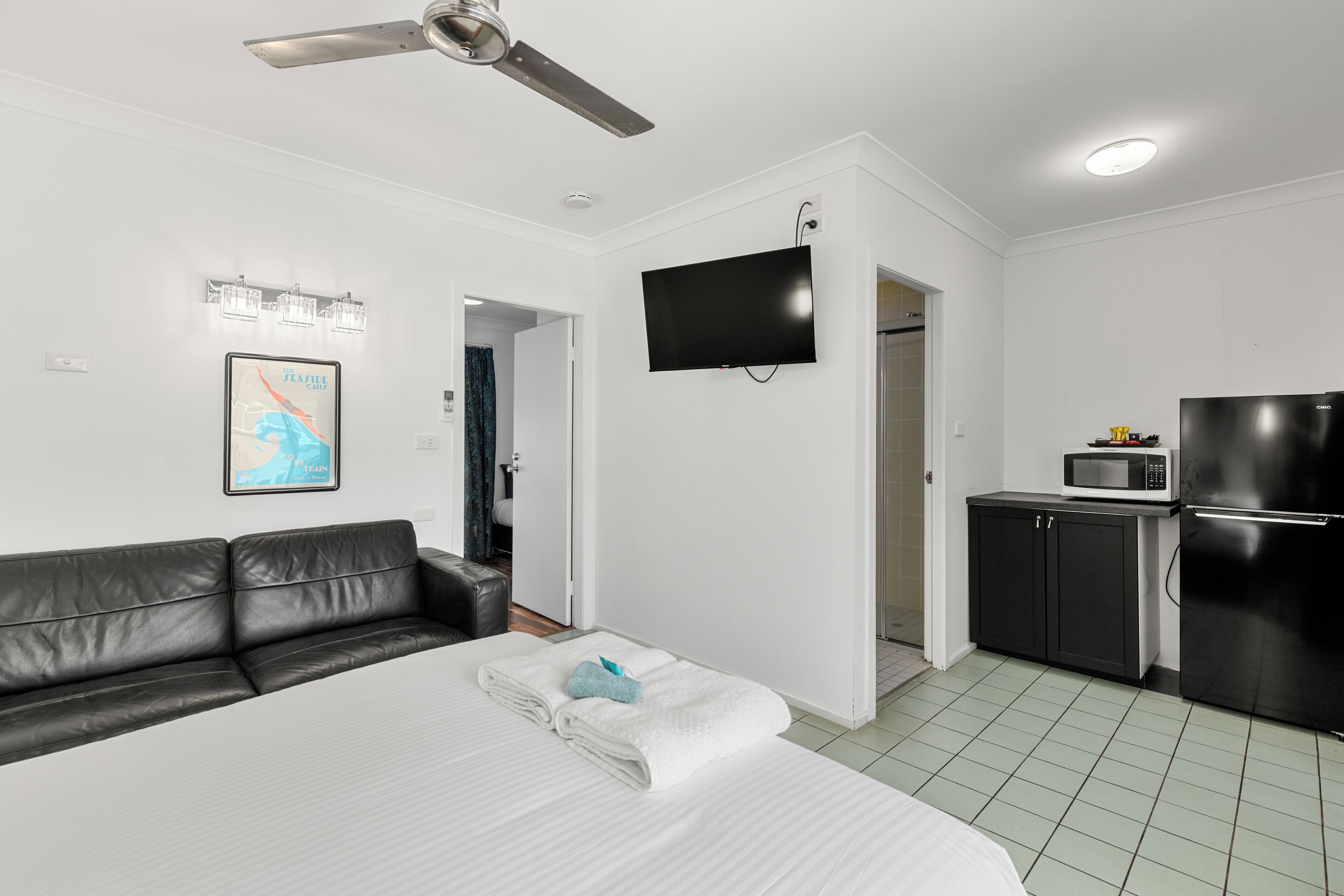 A modern hotel room with a bed, a black leather sofa, a flat-screen TV, a microwave, and a refrigerator.
