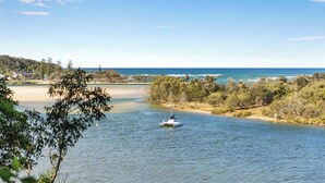 Une rivière où navigue un voilier, entourée d’arbres et bordée d’une plage lointaine.