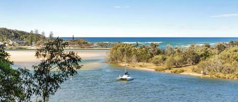 A river with a sailboat, surrounded by trees and a distant beach.