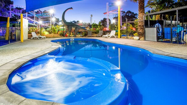 Una piscina con una estatua de dinosaurio, sillas de descanso y un área vallada con un tobogán de agua.